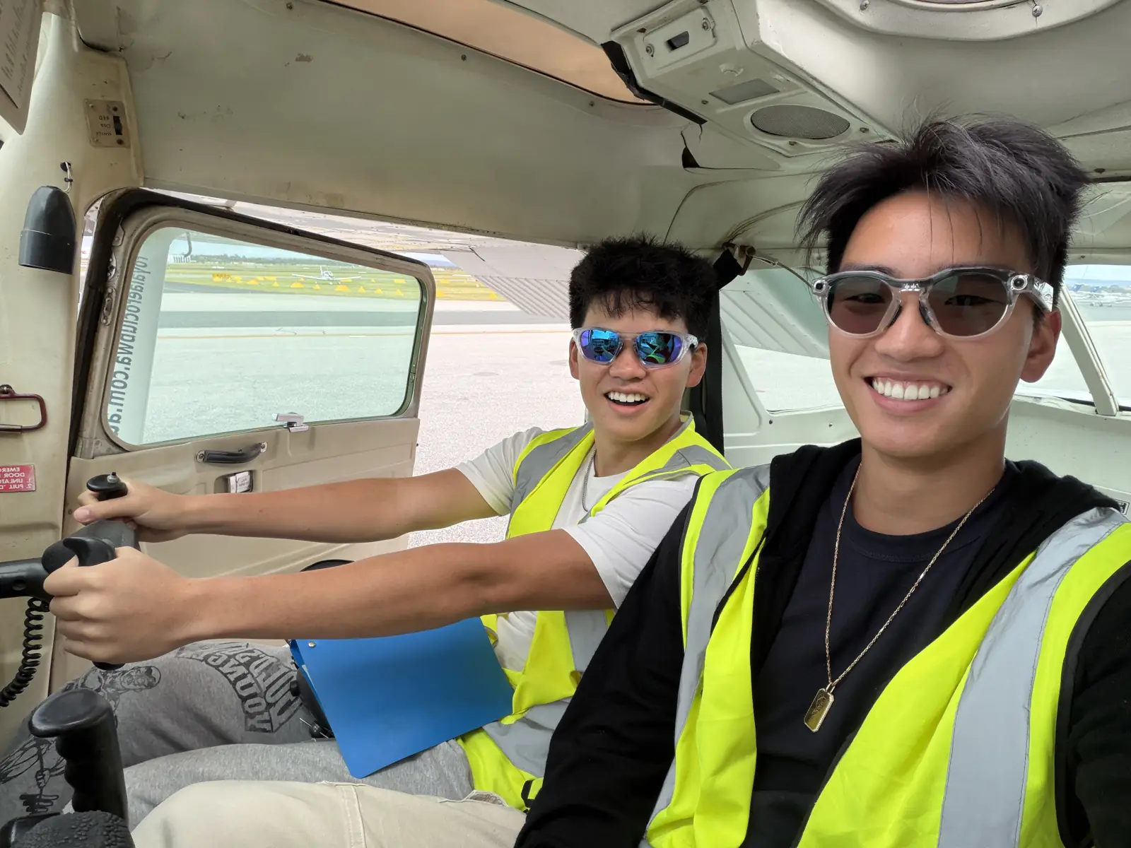 Two people smiling inside a light aircraft cockpit